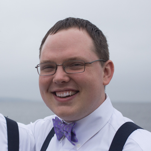 Photograph of Dan Bjorge, a smiling white male in his 30s with short brown hair wearing glasses and a purple bow tie